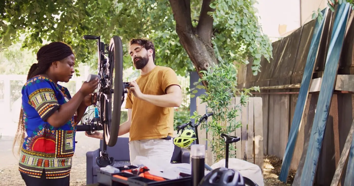 A healthy, determined multiracial pair in a yard repairing damaged bicycle components with a professional toolkit.
